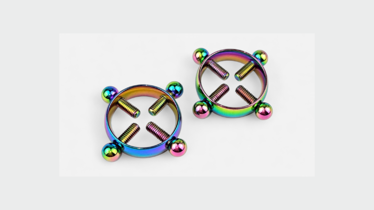 HU: Csöcscsavar szivárványos mellbimbóbilincs pár, négy állítható csavarral, elölnézetben világosszürke háttéren. EN: Titty Torque rainbow nipple clamp pair with four adjustable screws, front view on a light grey background.